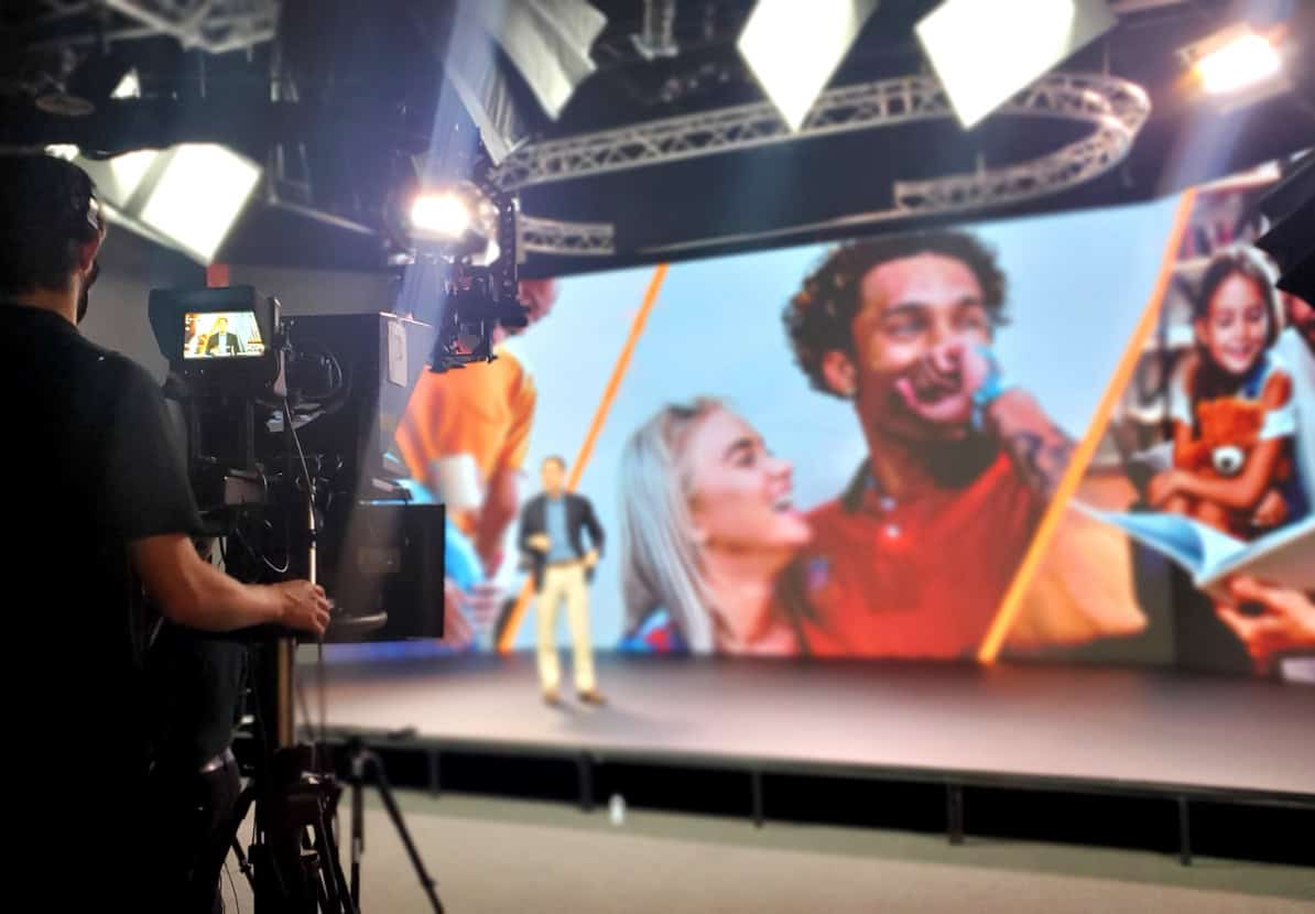 High-quality video production at TriVision Studios showcasing a large LED screen with vibrant visuals, professional filming equipment, and a crew capturing an event or presentation in a modern studio environment.