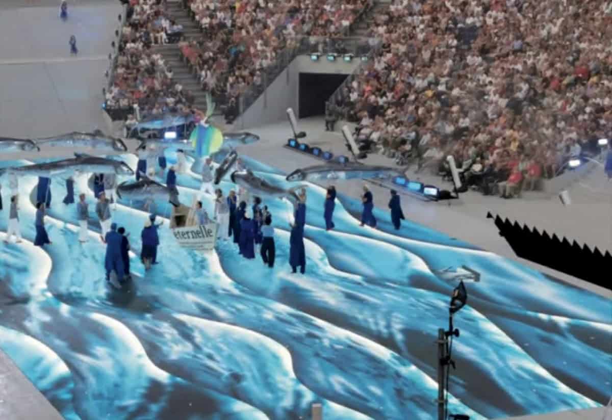 Lightning and water-themed stage production at a large indoor arena, featuring an elaborate water screen, performers in blue costumes, and a vast audience, showcasing advanced event staging and visual effects.