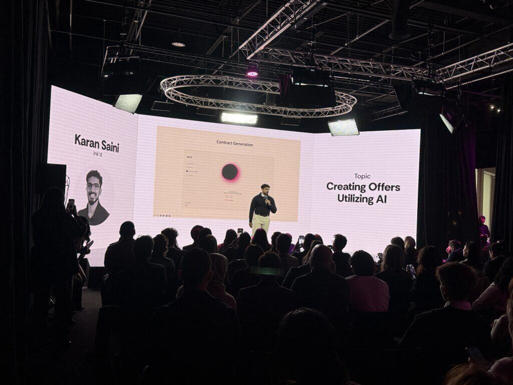 AI-powered presentation on creating offers utilizing artificial intelligence at TriVision Studios. Audience attentively listening to expert speaker on stage with large digital screen.