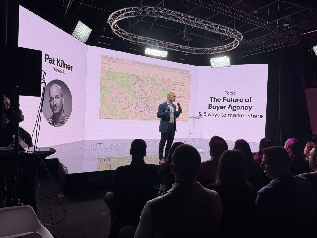 - High-tech stage with large LED screen displaying a speaker presenting on the future of buyer agency and market share strategies at a professional conference.
