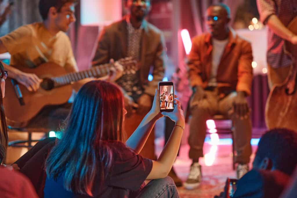 Live musical performance at TriVision Studios featuring artists with guitars, vibrant lighting, and audience capturing the moment on their phones for memorable entertainment experiences.