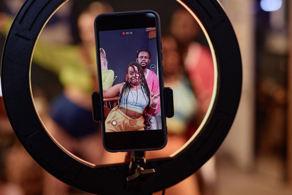 Young woman and man recording a video with a smartphone on a ring light, capturing vibrant indoor content with professional video production quality.