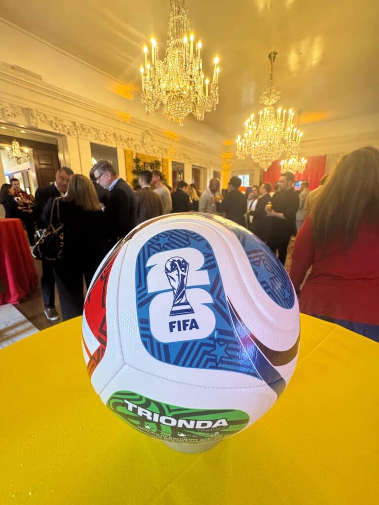 Vibrant soccer ball with FIFA logo showcased during a lively indoor event at a luxurious venue with grand chandeliers and elegant decor, highlighting professional event production by TriVision Studios.