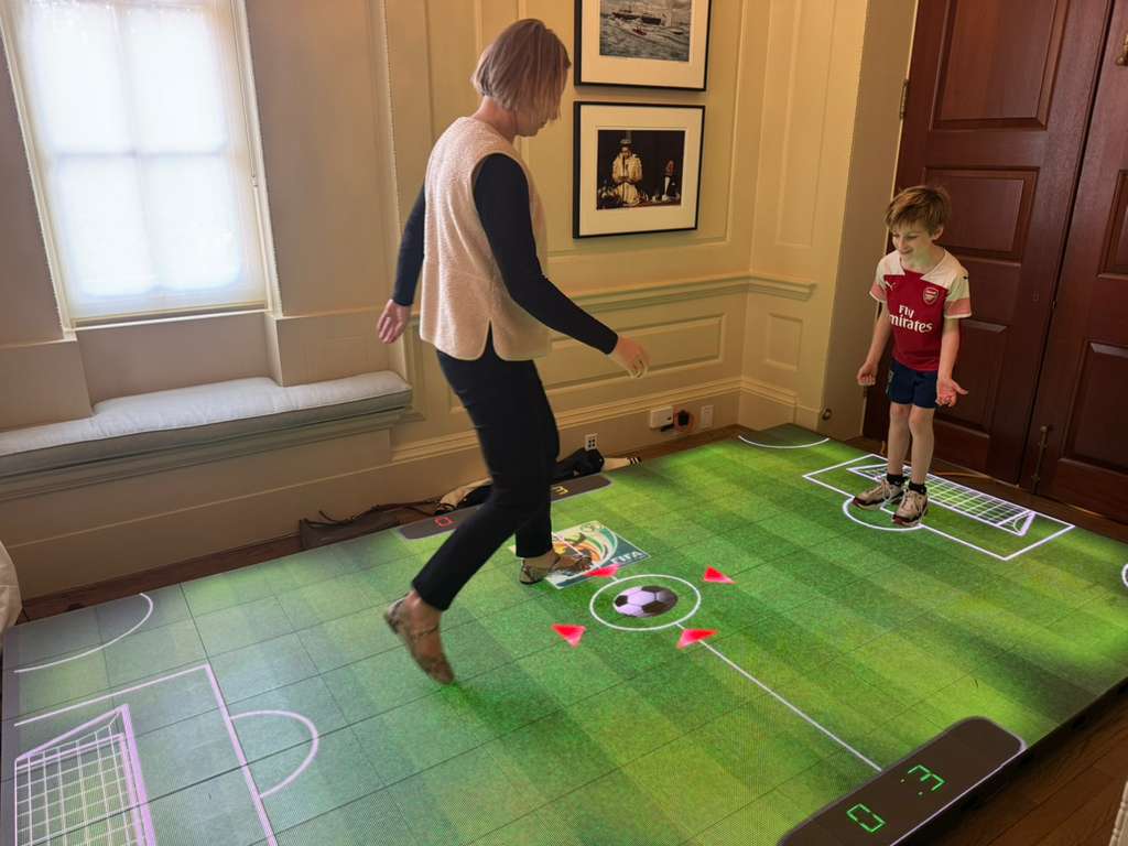 Ultra-wide projector displaying a soccer-themed interactive game on a wooden floor, providing immersive sports experience and innovative entertainment in a home or event setting.
