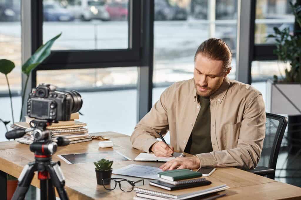 A man working on a project at a modern office desk with camera gear, notebooks, and a laptop, representing professional creative studio production by TriVision Studios.