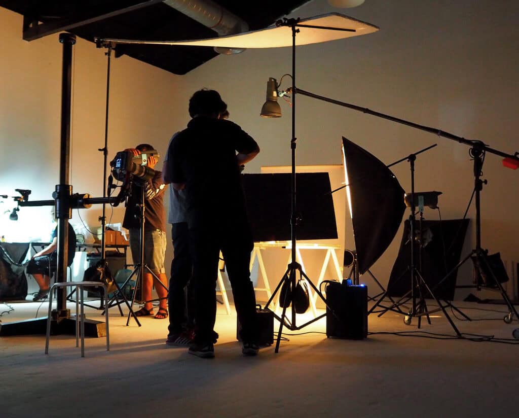 A behind-the-scenes shot of a film or video production studio featuring crew members setting up lighting and camera equipment for a professional shoot at TriVision Studios.