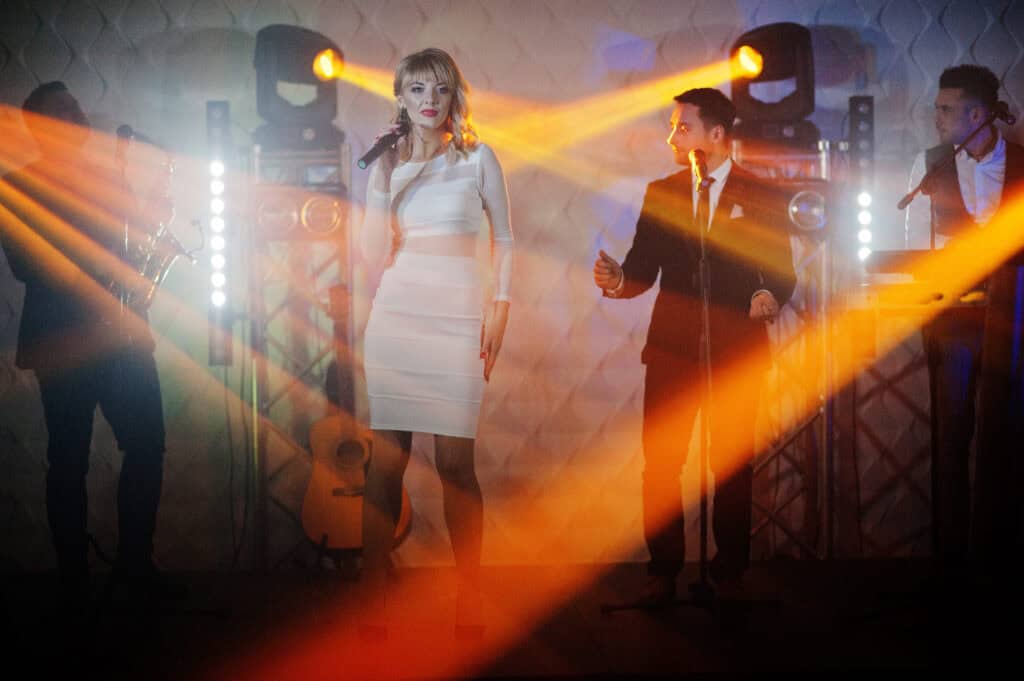 Elegant woman singer performing on stage with a band and vibrant lighting effects.