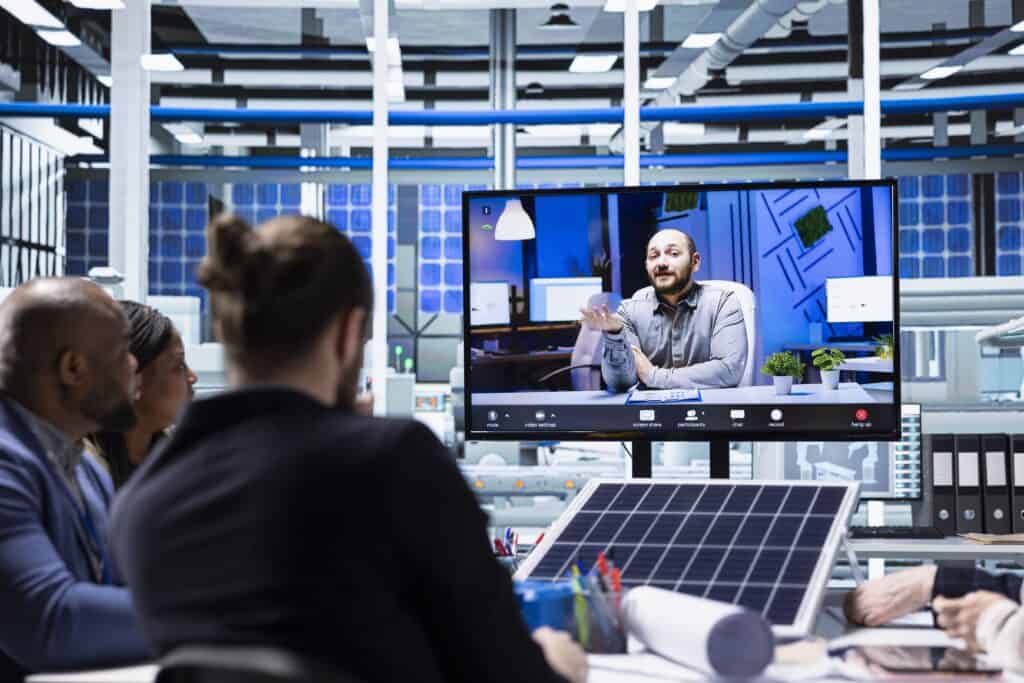 Business team participating in a virtual meeting about smart factory automation, with a large screen displaying a presenter and industrial equipment in the background.