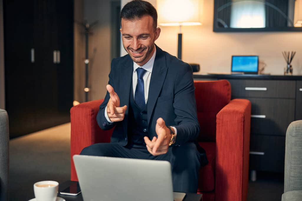 Professional businessman in a suit engaging with a laptop during a virtual meeting in a modern office setting.